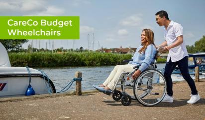 Man pushing a woman in a wheelchair by a river with a boat moored