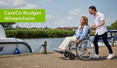 Man pushing a woman in a wheelchair by a river with a boat moored