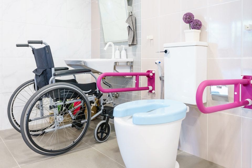 wheelchair at bathroom basin and toilet with hand rails